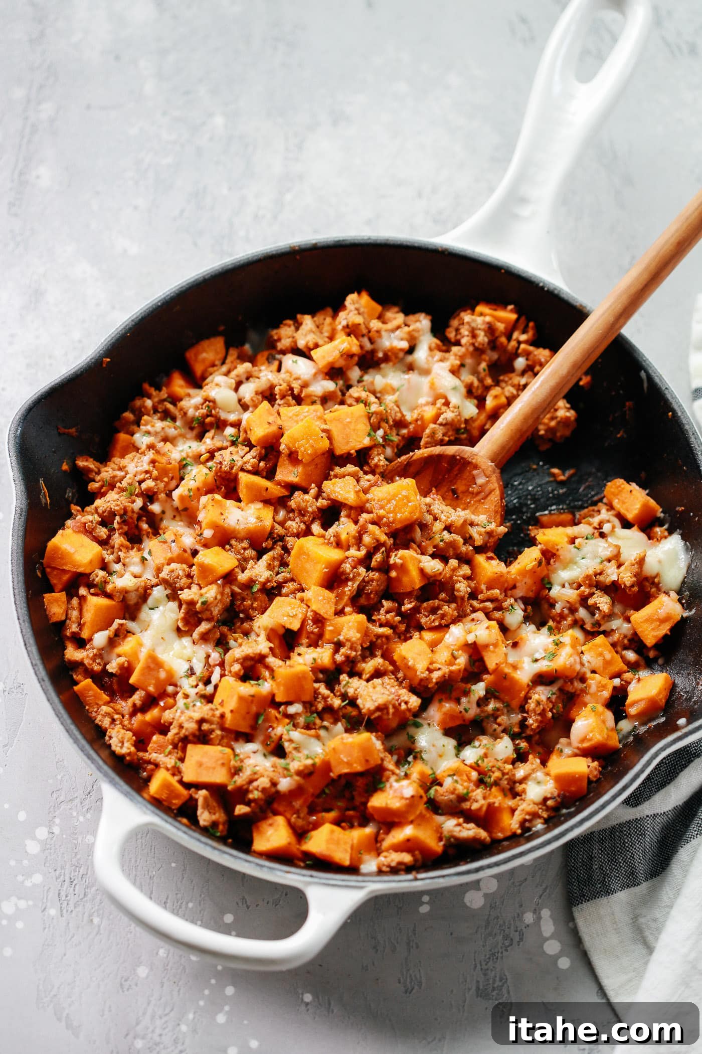Overhead view of a white skillet containing perfectly cooked ground turkey and sweet potato cubes