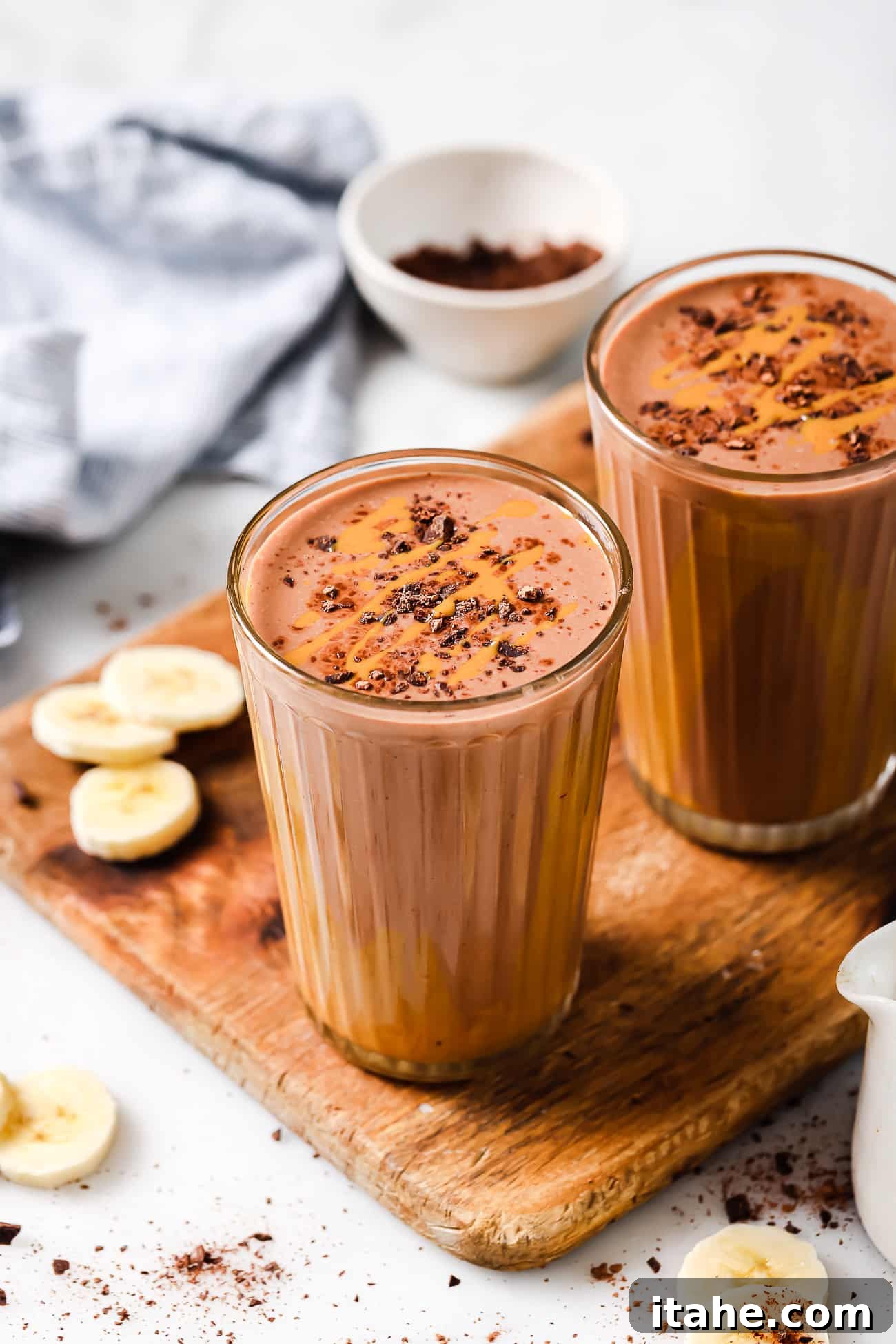 Two glasses of peanut butter chocolate smoothies on a wooden cutting board, ready for serving.