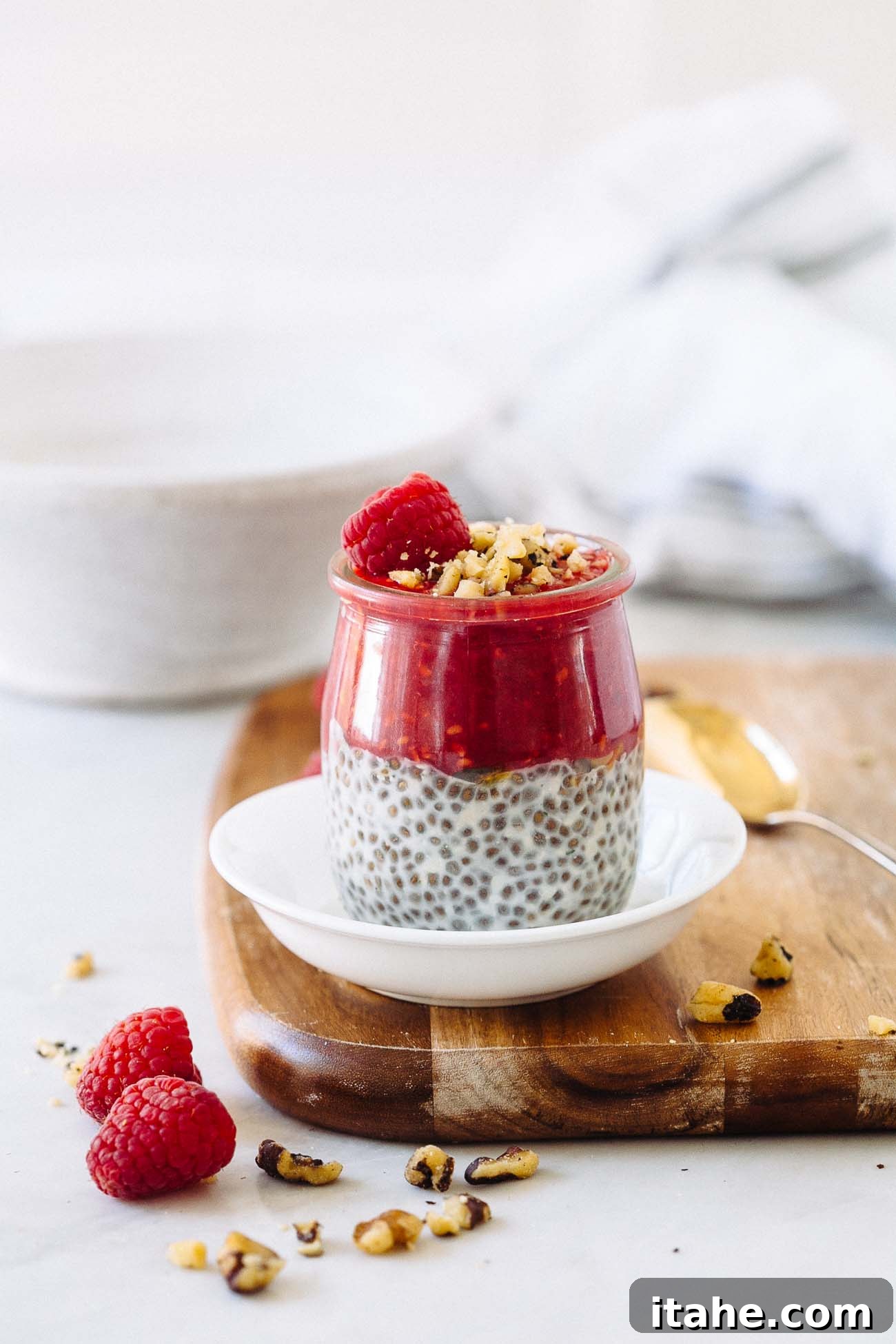 A jar of chia seed pudding with raspberry puree, raspberry, and walnuts on top.