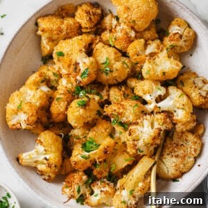 A close-up of a serving of Roasted Cauliflower with Parmesan and Garlic, garnished with fresh herbs in a white bowl.