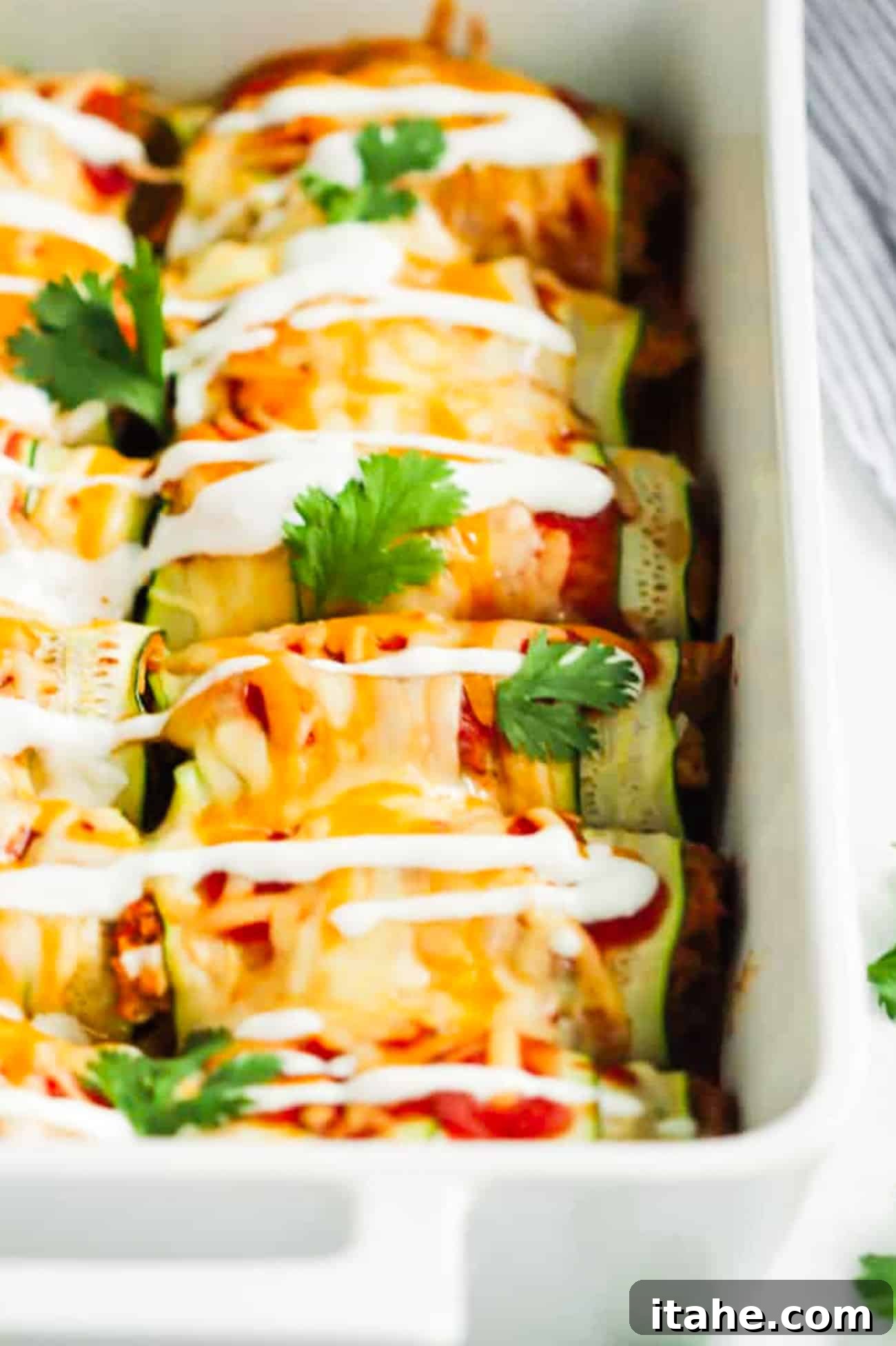 A large white baking dish showcasing a fully baked batch of zucchini chicken enchiladas, featuring a golden, melted cheese topping, ready for serving.