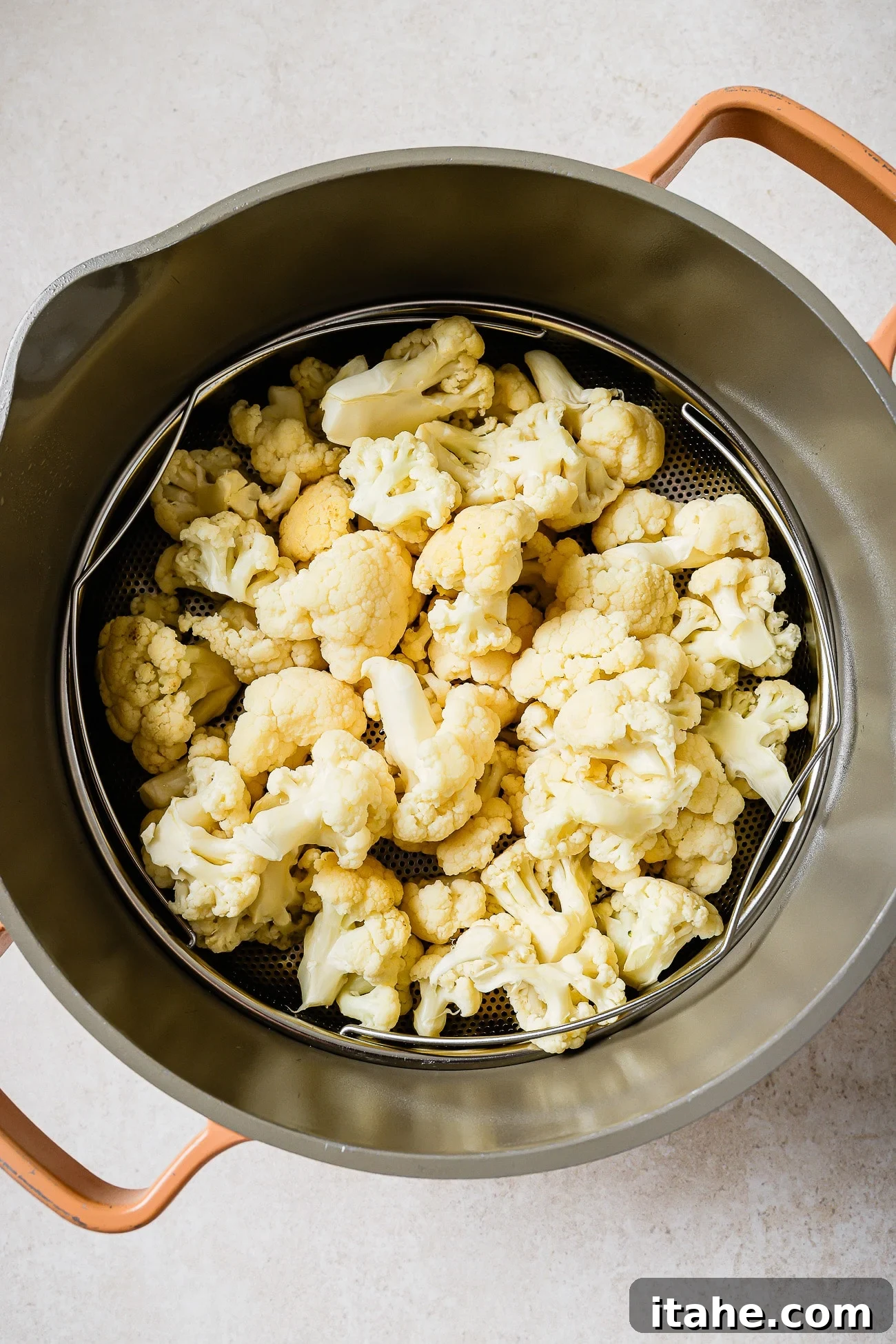 Cauliflower florets in a steamer basket inside of a large pot. 