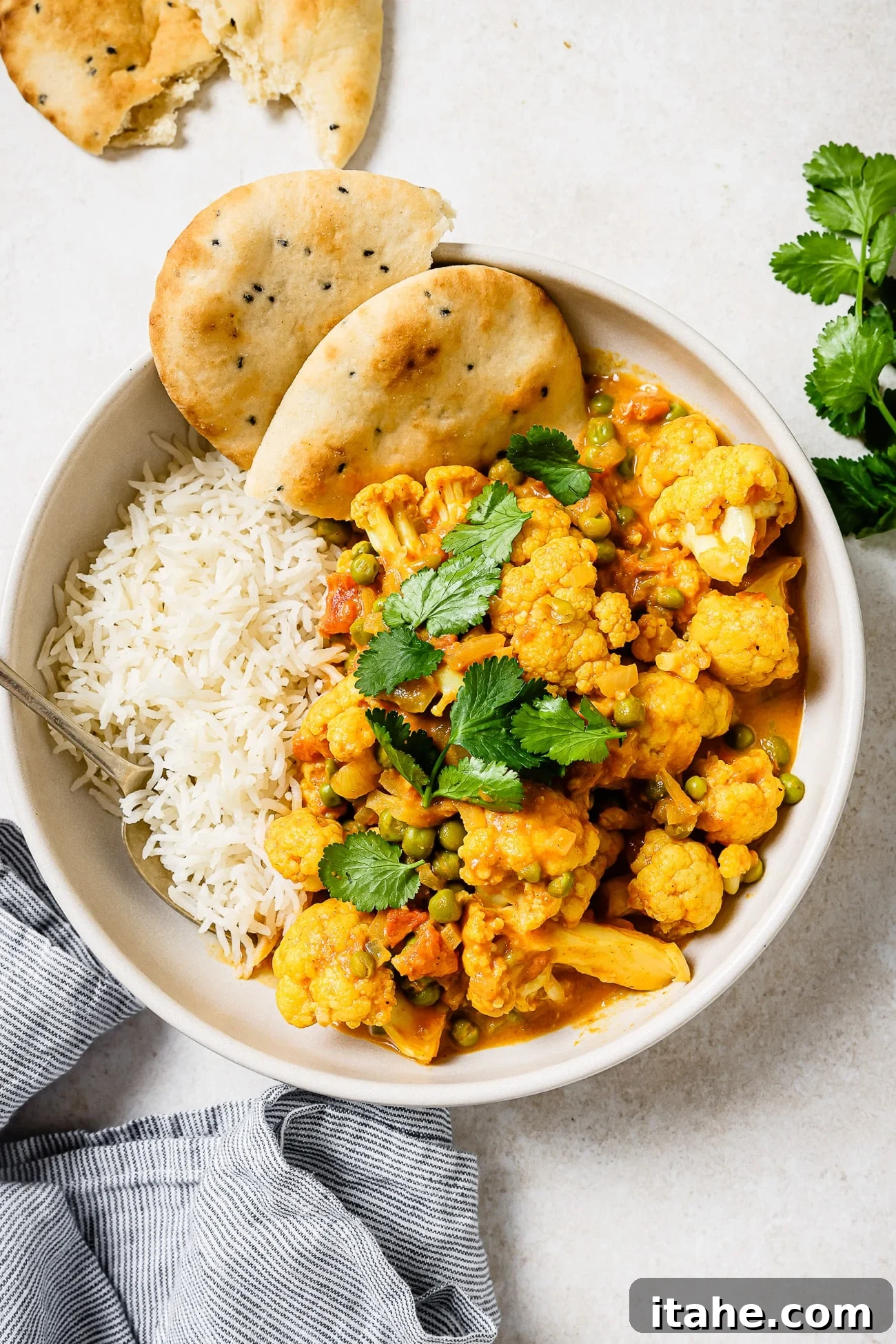 Cauliflower curry in a bowl with rice and a side of naan. 