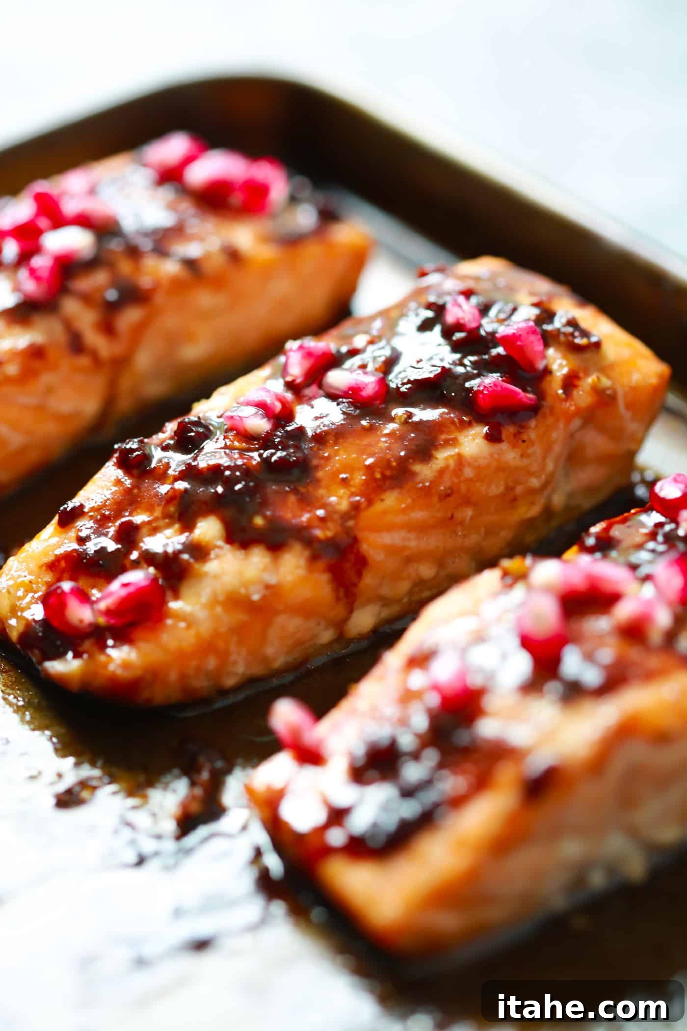 The easiest Pomegranate Glazed Salmon you will ever make. It only requires 4-ingredient and the glaze has no added sugar, but has a delicious tangy flavor! Close-up view of three salmon fillets arranged on a baking sheet, coated with a luscious pomegranate glaze.