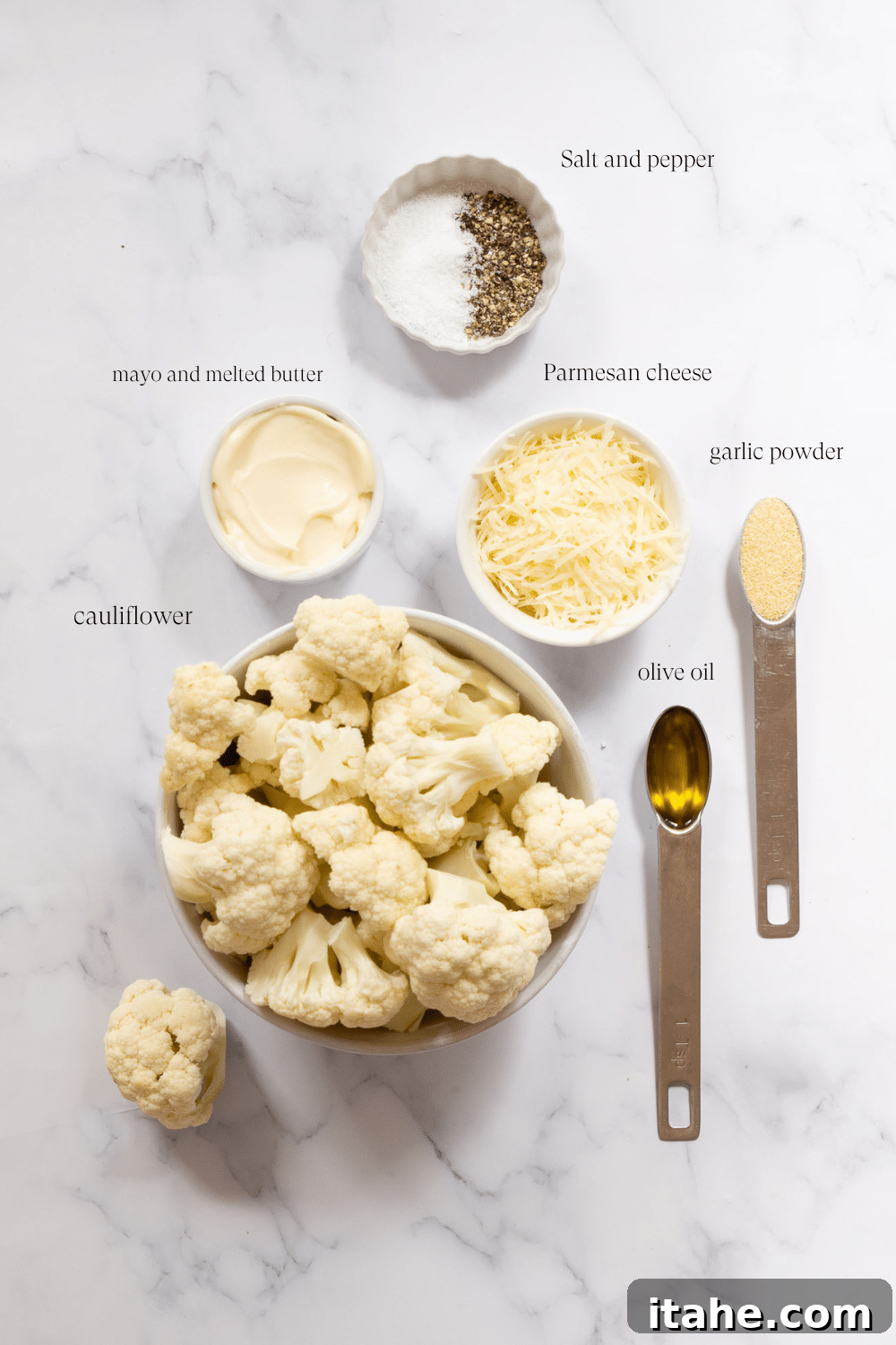 Ingredients for creamy mashed cauliflower laid out on a marble countertop, including fresh cauliflower, butter, mayonnaise, and parmesan cheese.