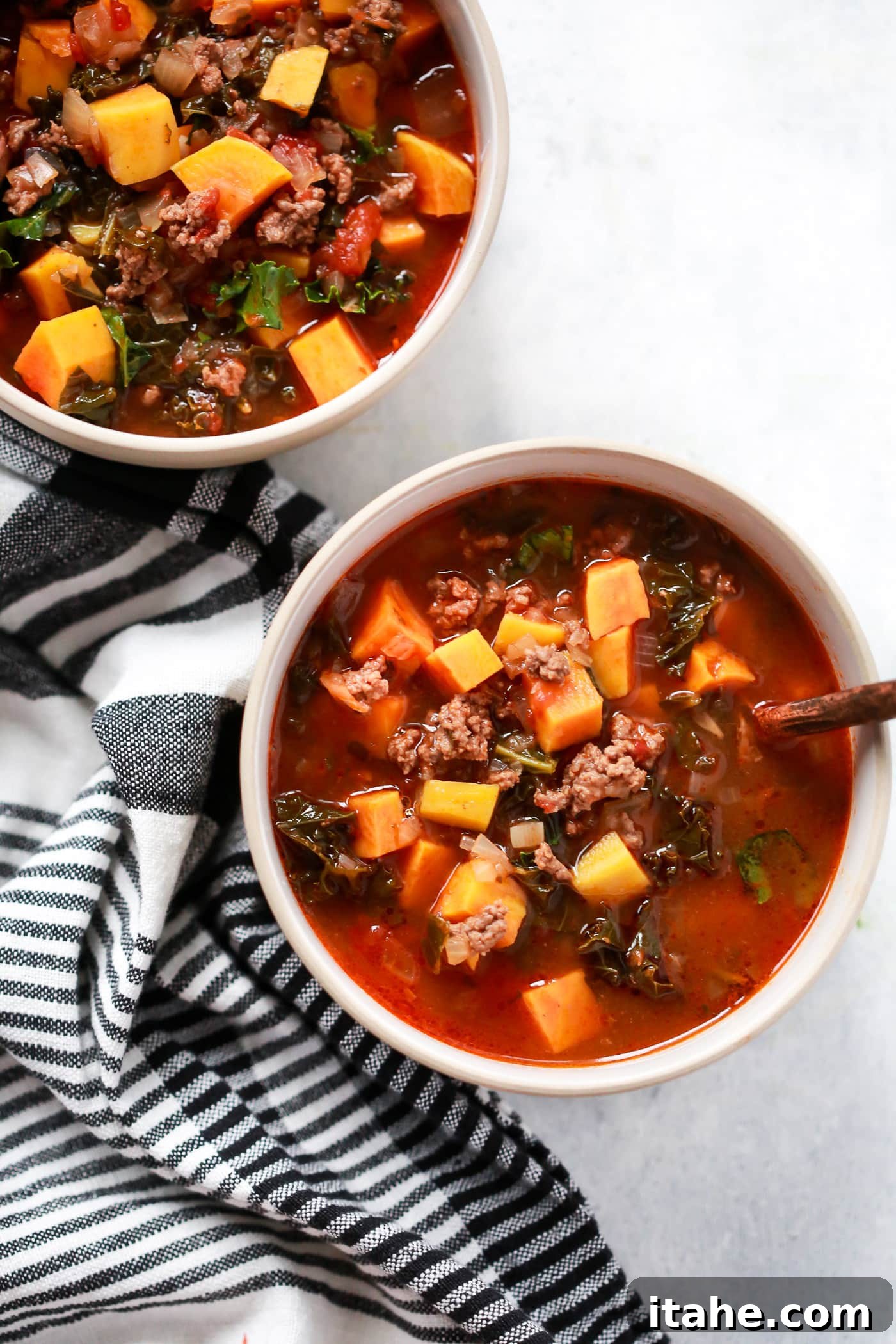 overhead view of two bowls containing Ground Beef Butternut Squash Kale Soup, garnished with fresh herbs