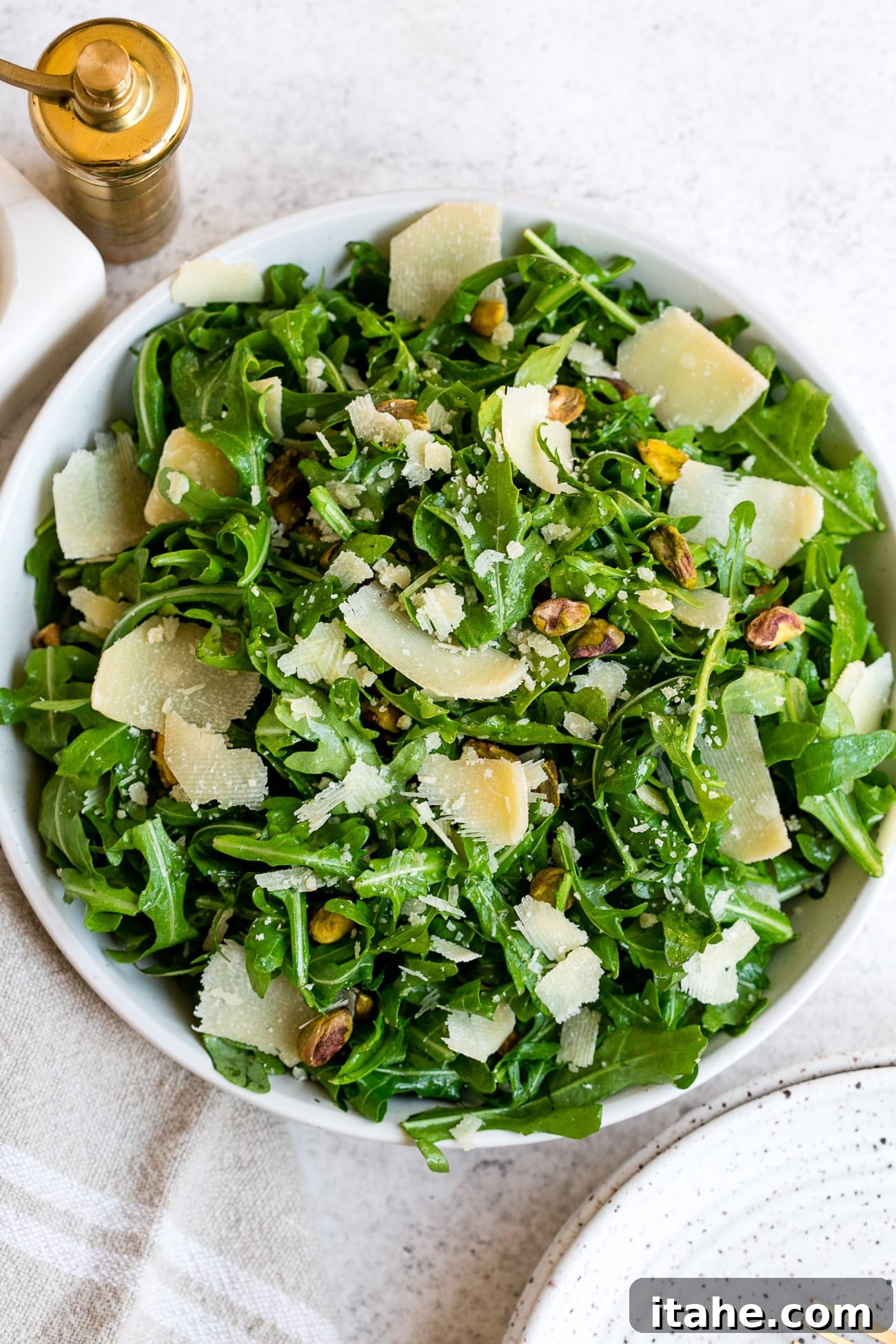 Fresh & Filling Low-Carb Lunches 17 Overhead view of a fresh Arugula Salad with Parmesan cheese and vinaigrette in a white bowl.