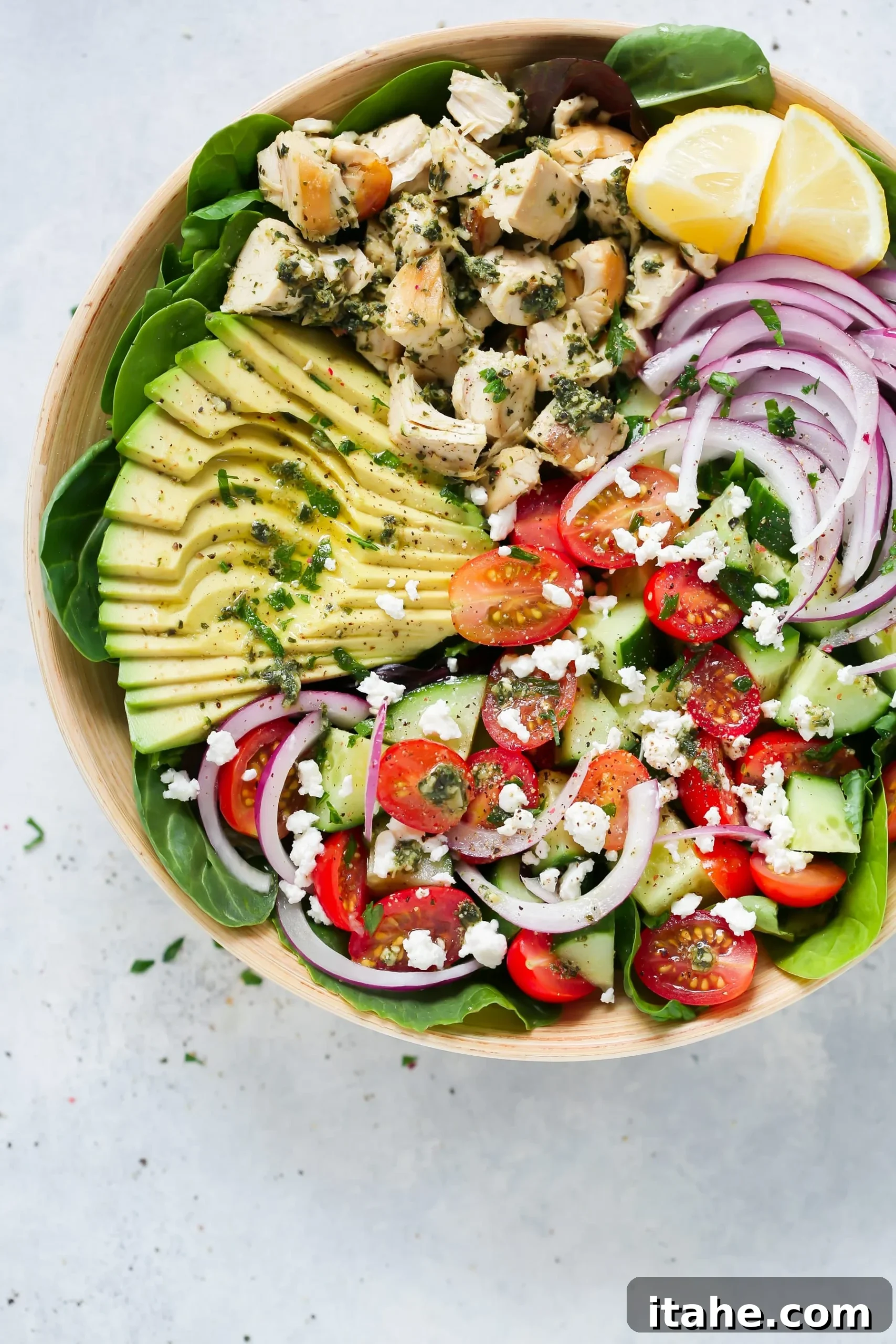 Fresh & Filling Low-Carb Lunches 3 Overhead view of a vibrant Pesto Chicken Salad served in a rustic wooden bowl, garnished with fresh herbs.