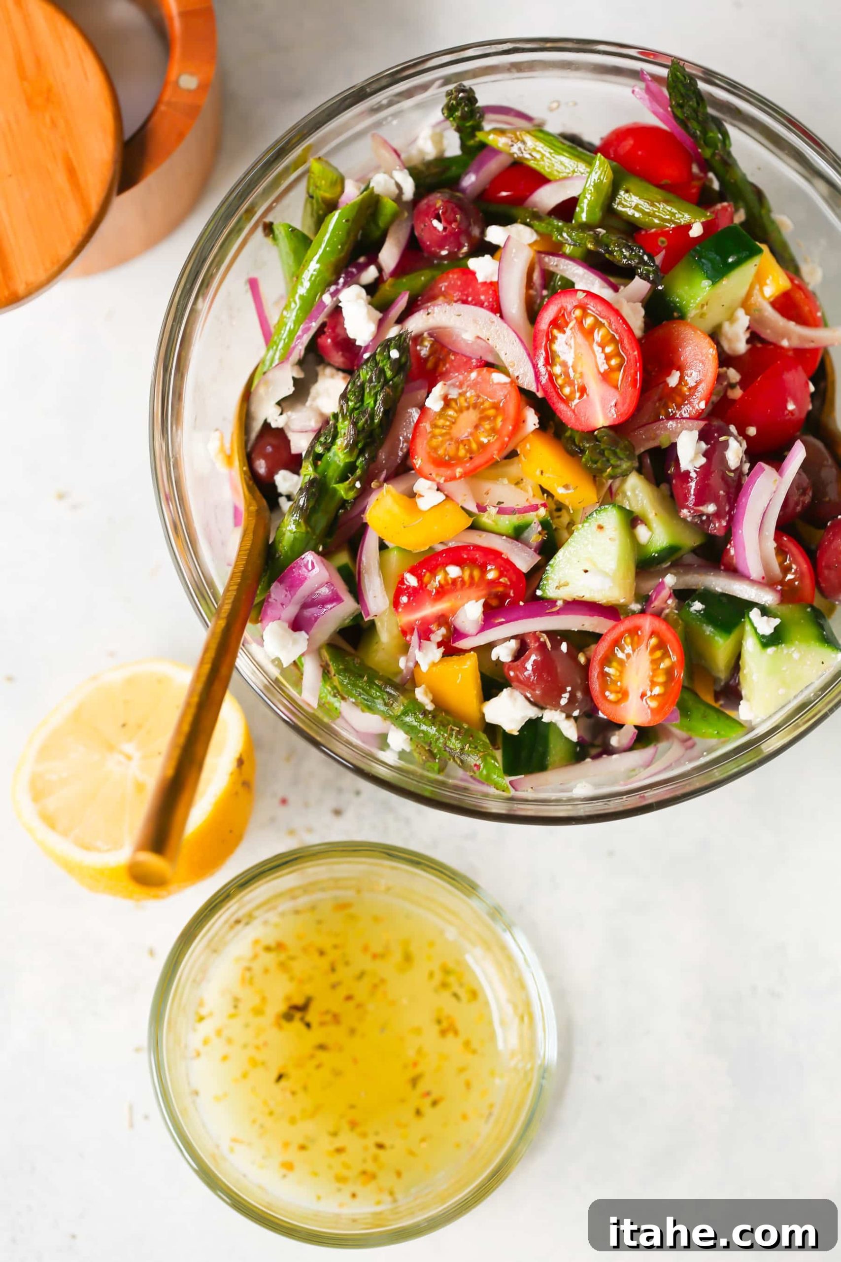 Fresh & Filling Low-Carb Lunches 4 Overhead view of a fresh Asparagus Greek Chopped Salad in a clear glass bowl, featuring vibrant greens and vegetables.