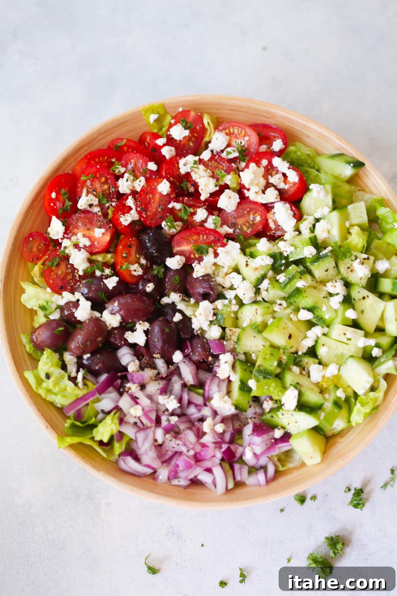 Fresh & Filling Low-Carb Lunches 6 Overhead view of a rustic wooden bowl filled with Easy Mediterranean Chopped Salad, featuring olives, tomatoes, and greens.
