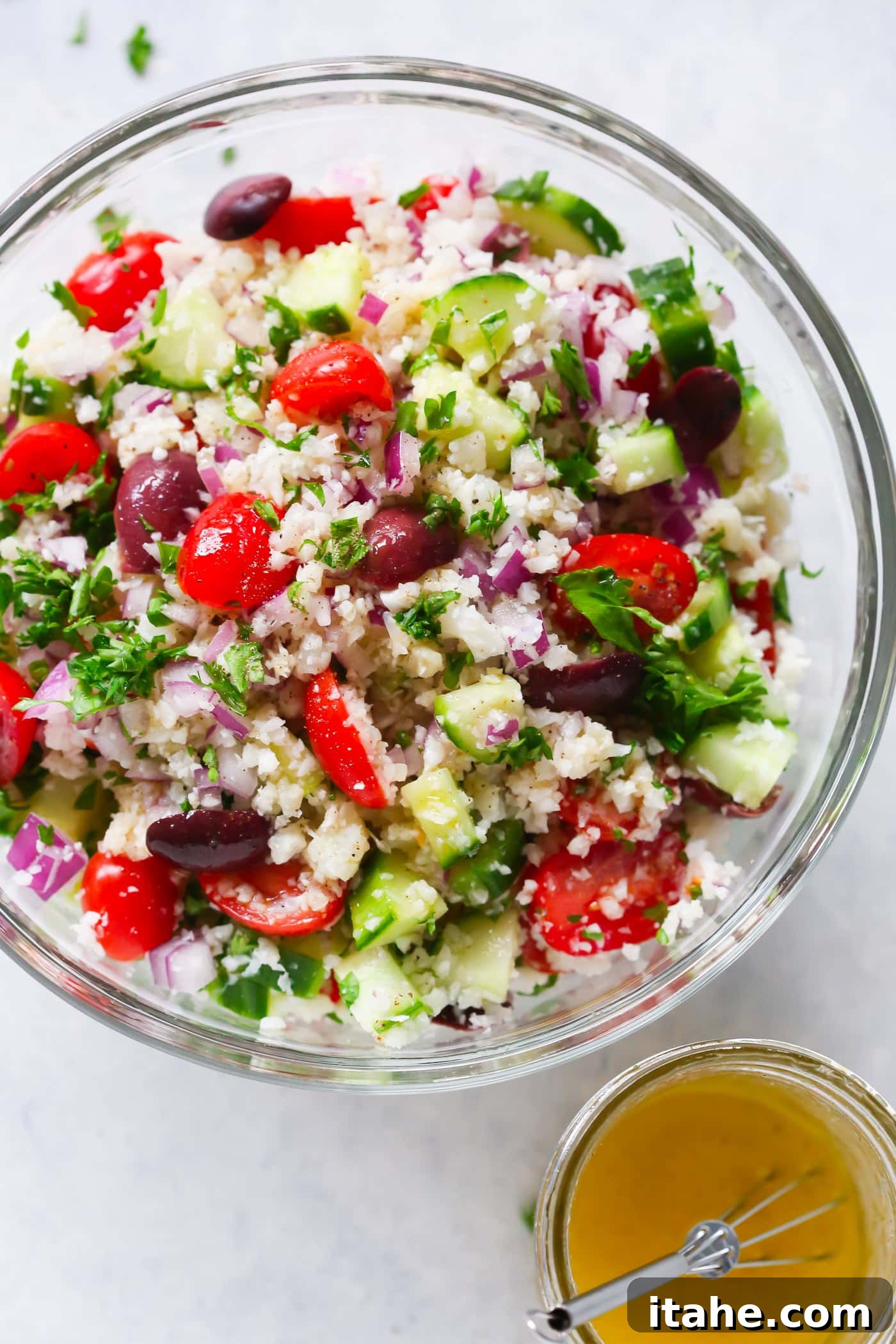 Fresh & Filling Low-Carb Lunches 10 A clear glass bowl containing a colorful Mediterranean Cauliflower Salad, with fresh herbs and vegetables.