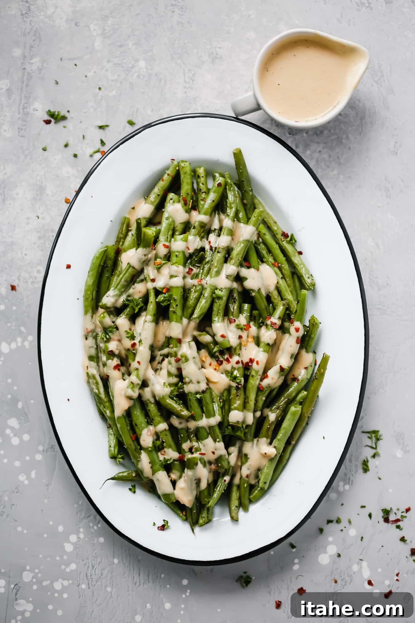 An oval serving platter with perfectly roasted green beans generously drizzled with spicy tahini sauce, garnished with fresh herbs.
