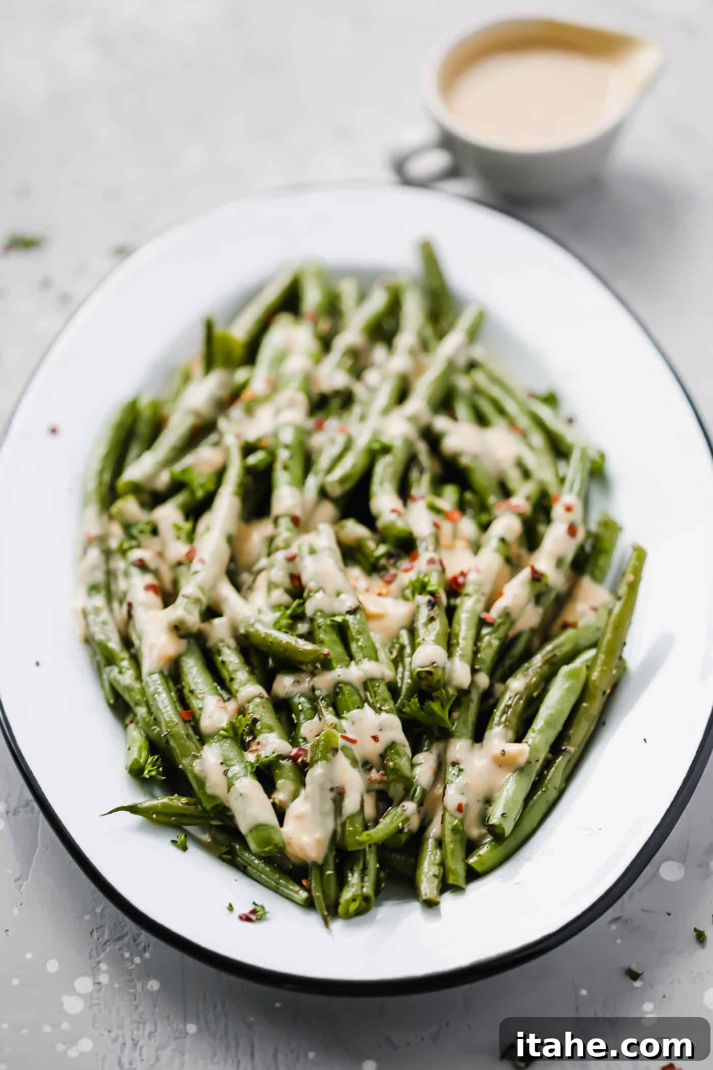 Overhead view of a white serving plate laden with roasted green beans generously coated in a creamy, spicy tahini sauce, ready to be served.