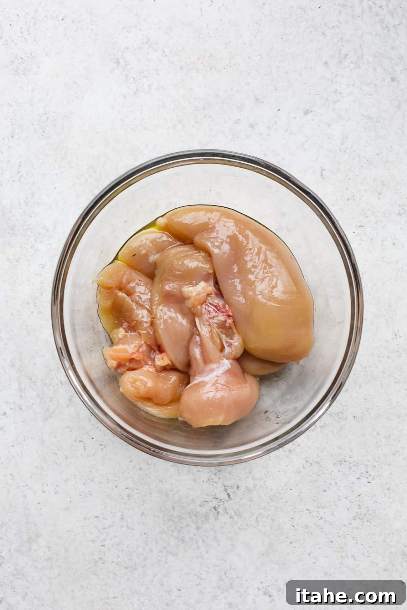 Flame-Kissed Chicken & Creamy Avocado Salad 3 Seasoning chicken breast in a large bowl, preparing it for grilling.