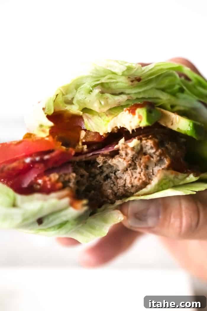 Delicious Bunless Burger Ideas 3 showing a hand holding a bunless burger after someone has taken a bite, revealing the juicy patty and fresh fillings.