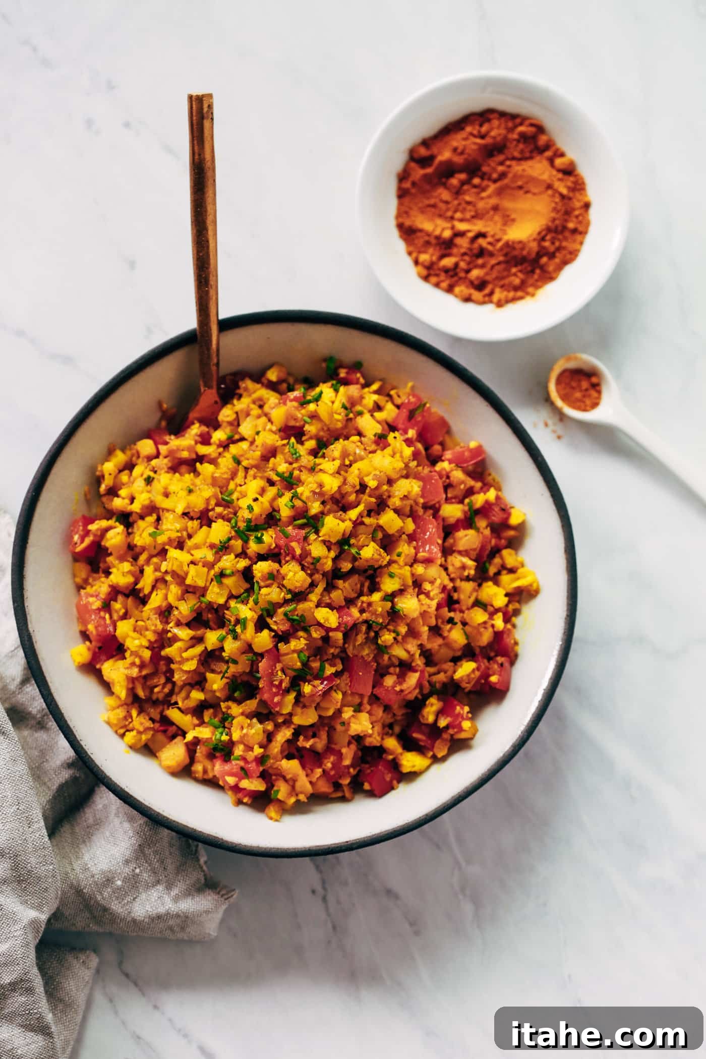 Overhead photo of a bowl of golden cauliflower rice, garnished with fresh chives.