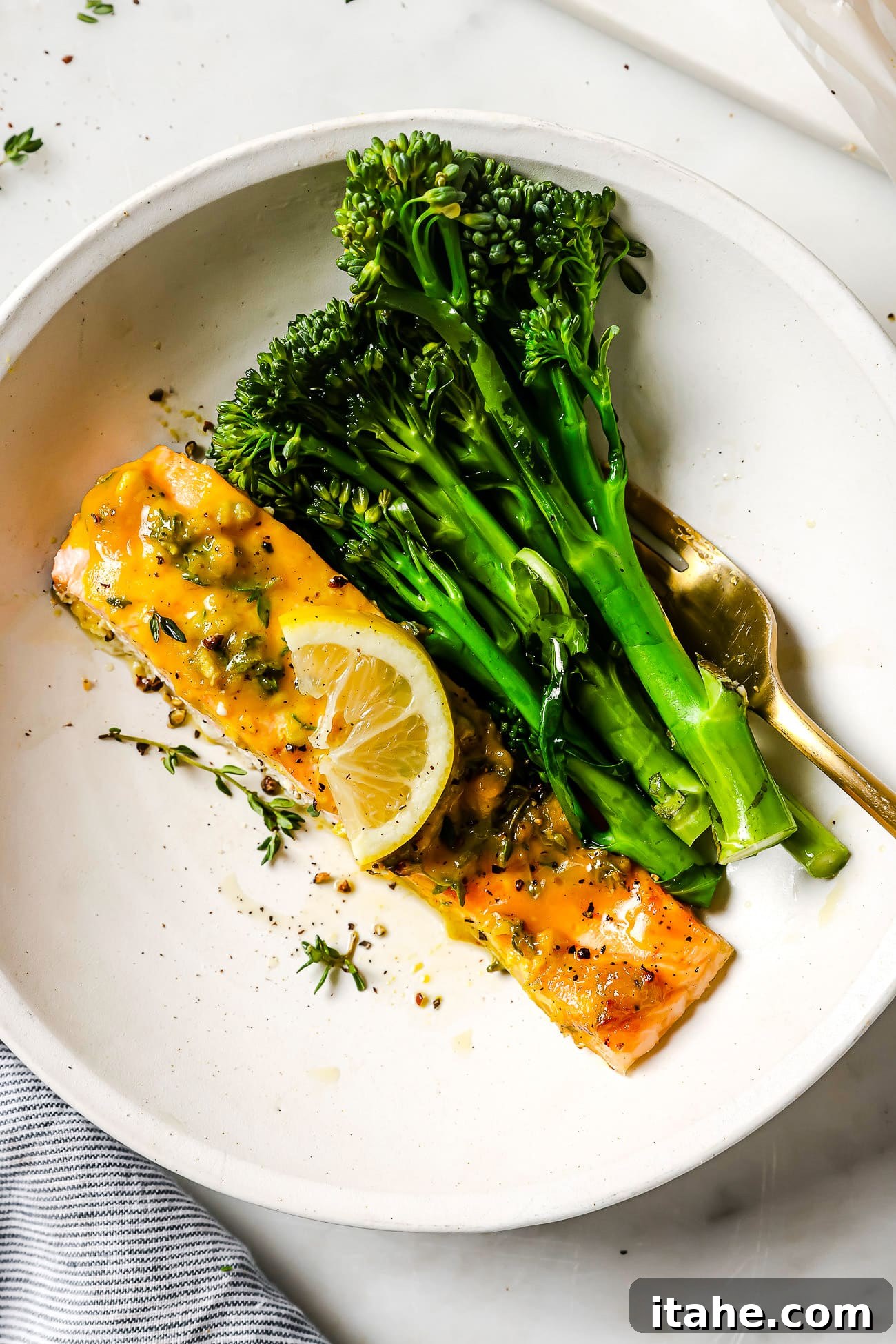 Maple mustard salmon on a white plate with broccolini and a lemon slice.