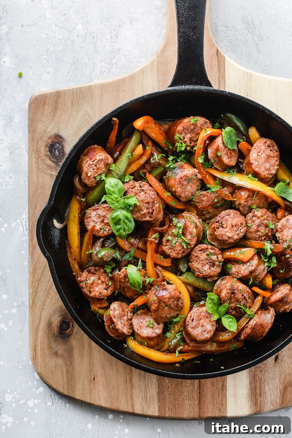 Italian Sausage, Onions and Peppers in a cast iron skillet, garnished with fresh herbs.