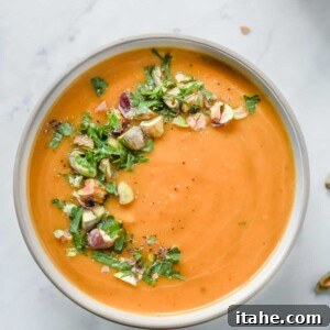 Overhead photo of a white bowl with butternut squash soup with garnish.