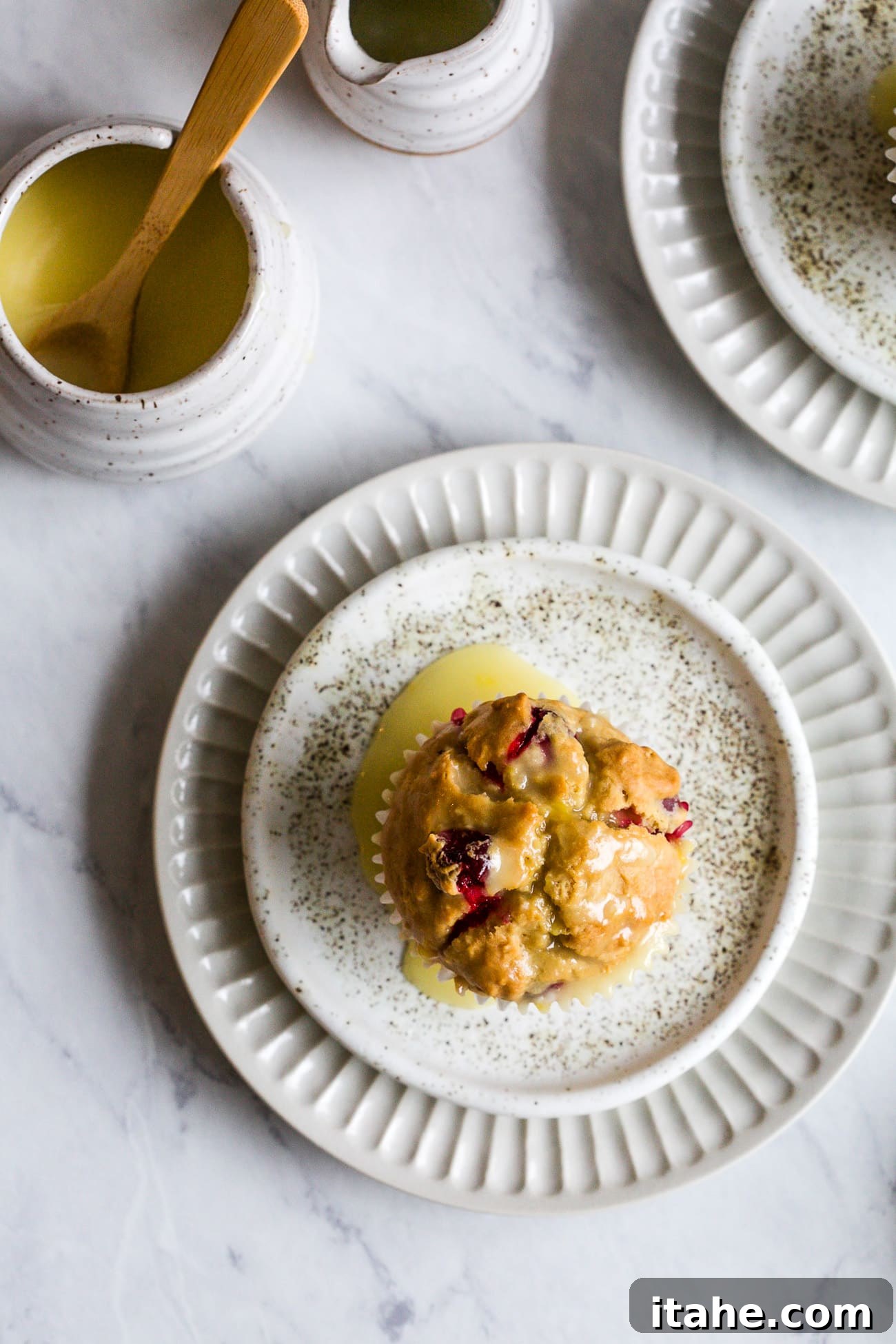 Cranberry muffin with orange glaze on a white serving plate. 