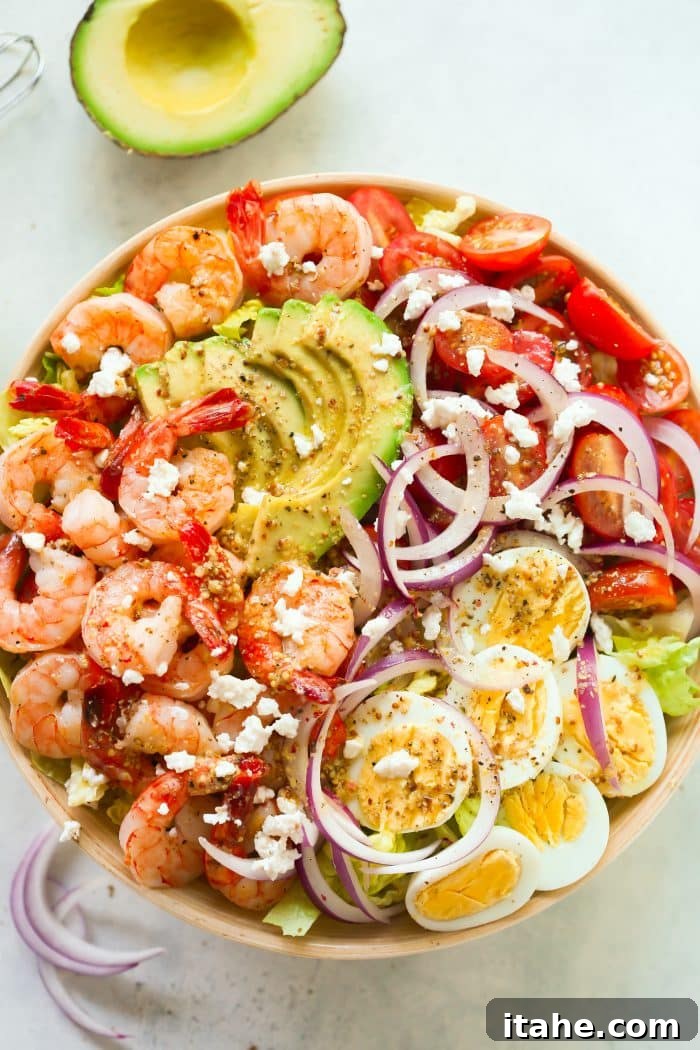 An overhead view of a colorful shrimp salad in a wooden bowl, featuring avocado, tomatoes, and hard-boiled eggs.