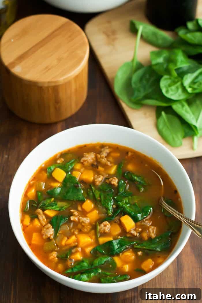 A close-up of a creamy sweet potato and spinach soup in a white bowl, garnished with fresh herbs.