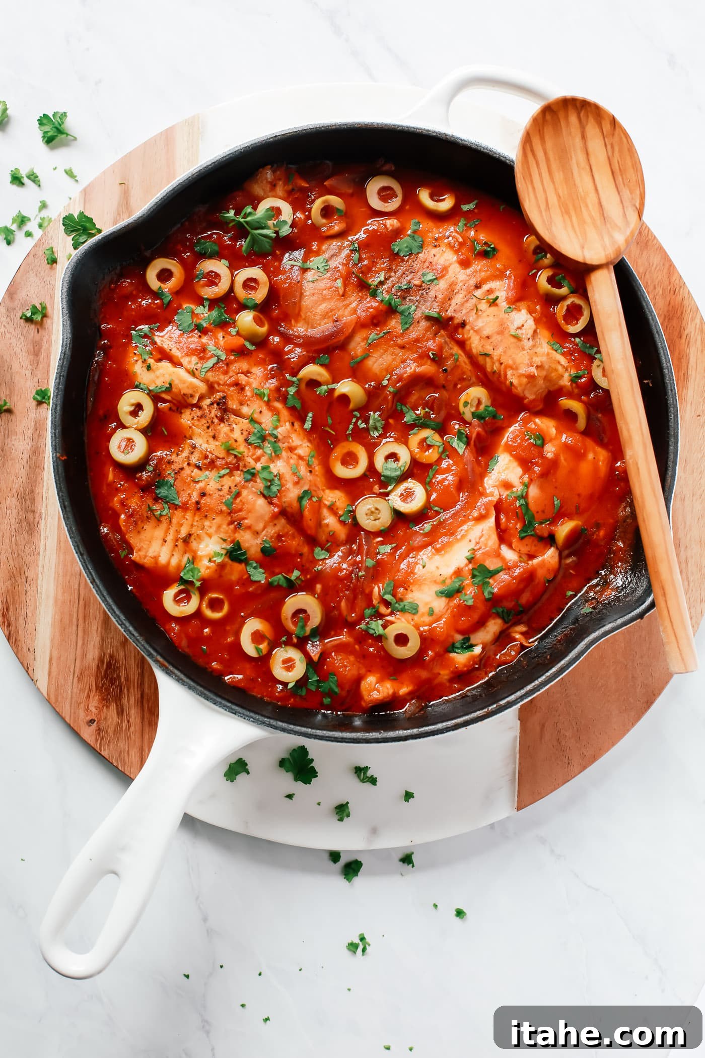 An overhead view of a white skillet presenting succulent tilapia fillets nestled in a vibrant tomato sauce, a simple and quick meal.