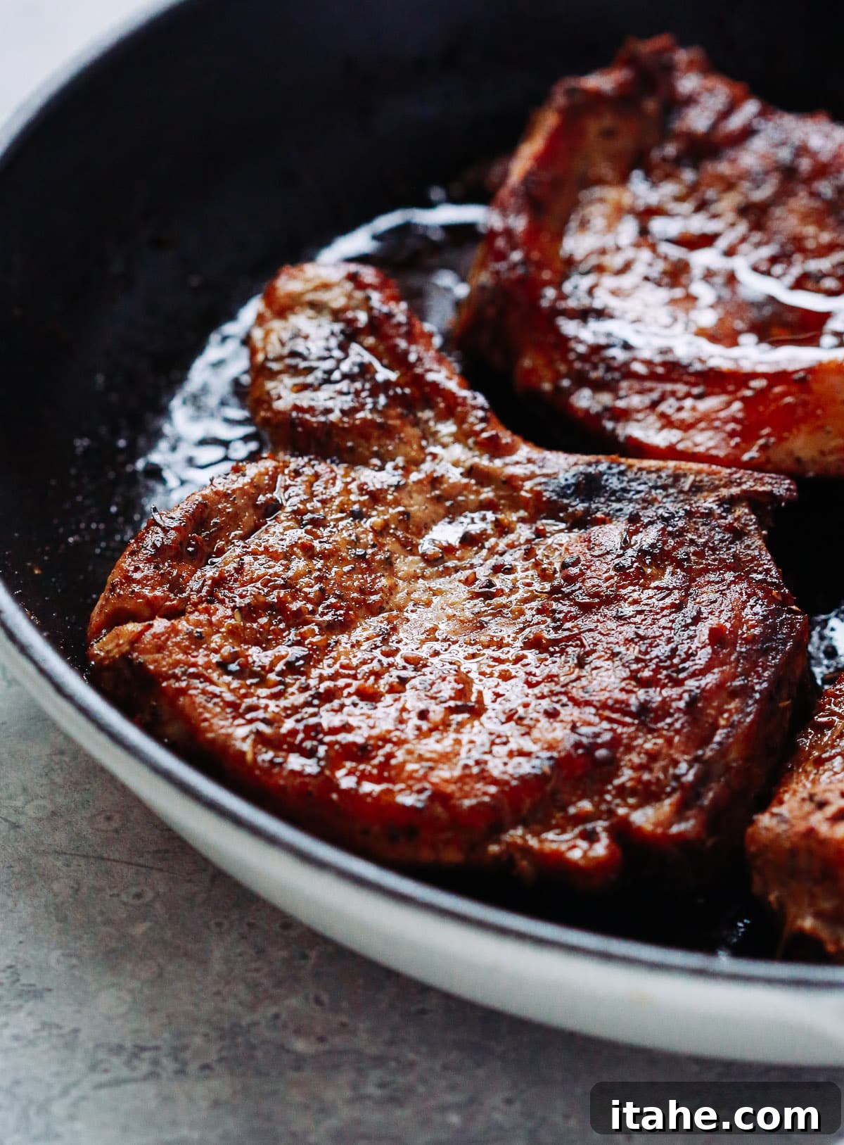close-up view of two cooked Oven Pork Chops in a white skillet, showing a beautiful crust