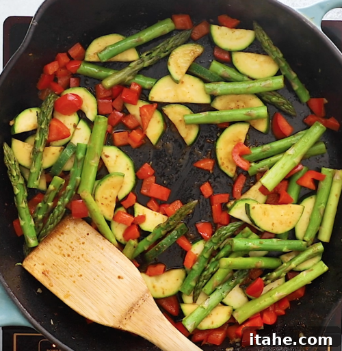 overhead view of a cast iron skillet containing mixed vegetables cooking