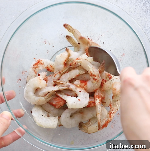 overhead view of a large glass bowl containing shrimp and spices for seasoning