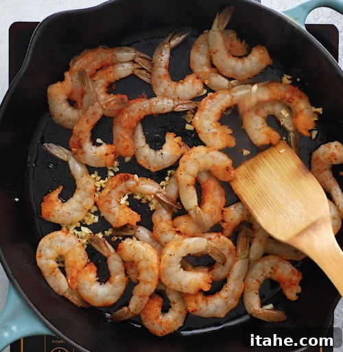 overhead view of cast iron skillet containing shrimp cooking with spices