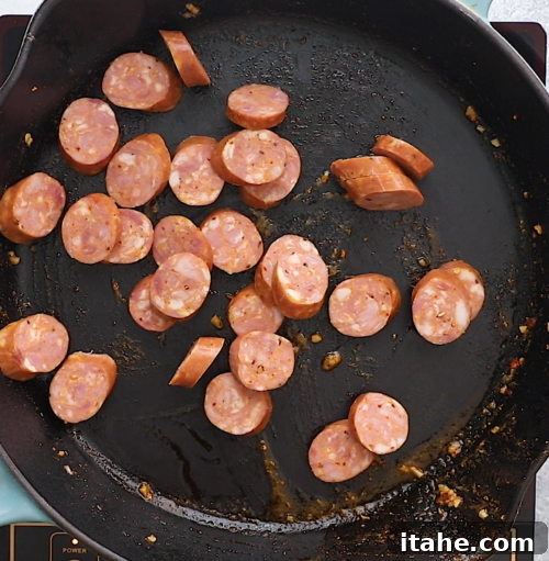 overhead view of a cast iron skillet containing sliced sausage cooking