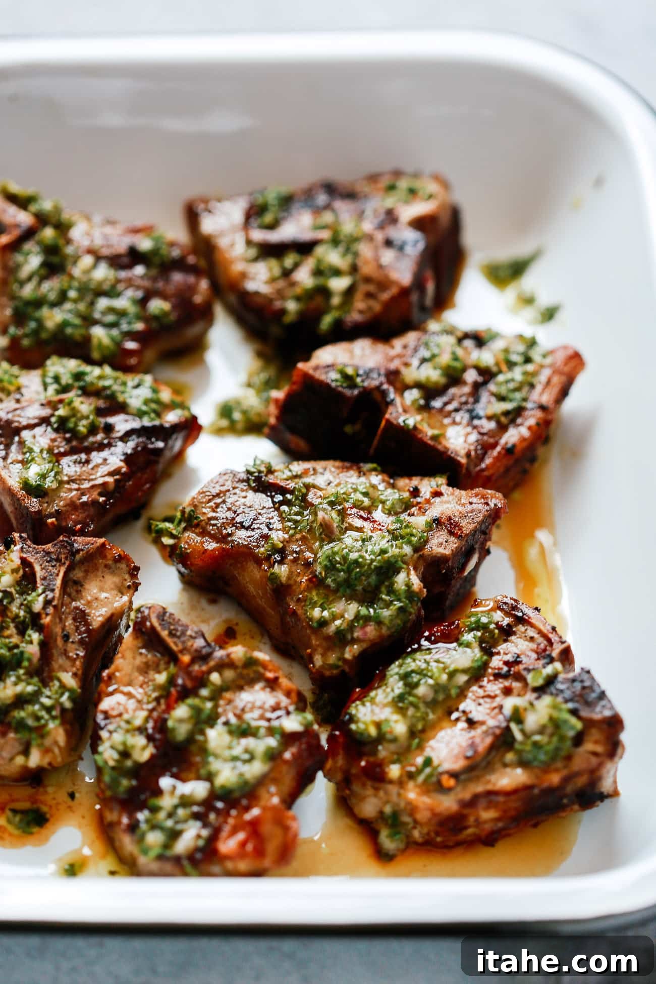 Close-up of perfectly seared lamb shoulder chops glistening with fresh chimichurri sauce.