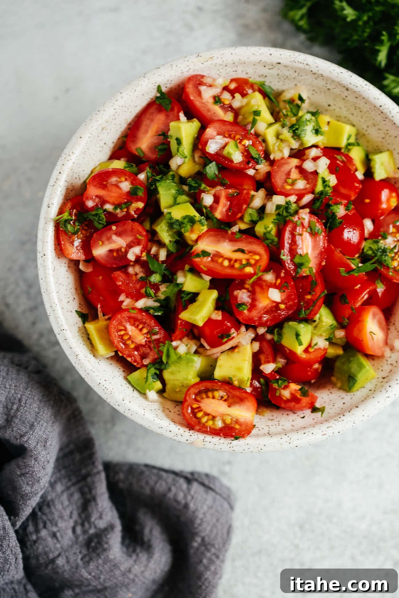 A close-up shot of a fresh avocado tomato salad, showcasing vibrant red tomatoes and green avocado chunks in a white bowl.