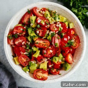 An overhead photo of an avocado tomato salad in a white bowl.