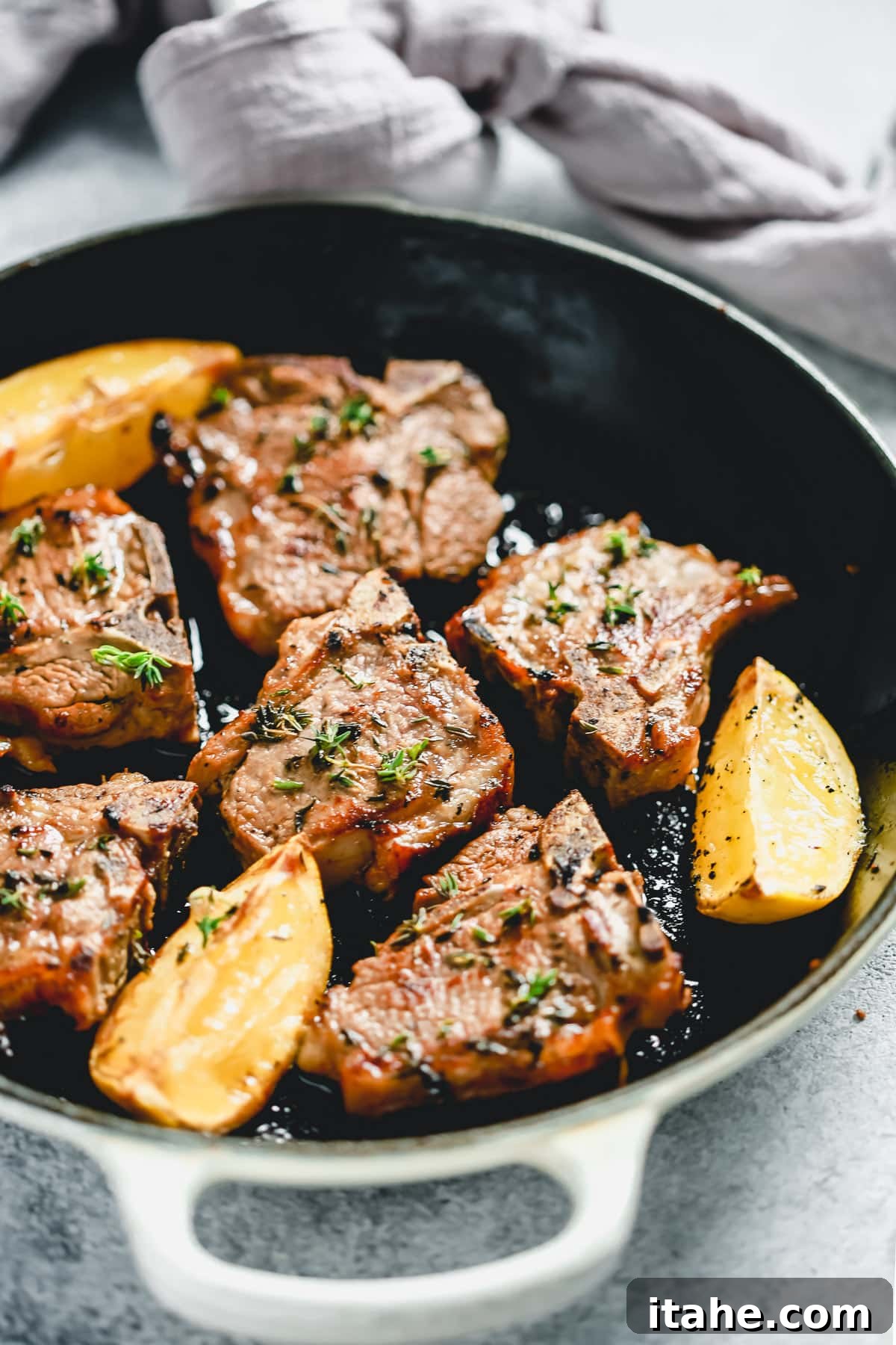 Cooked lamb chops in pan with fresh lemon wedges and sprigs of thyme