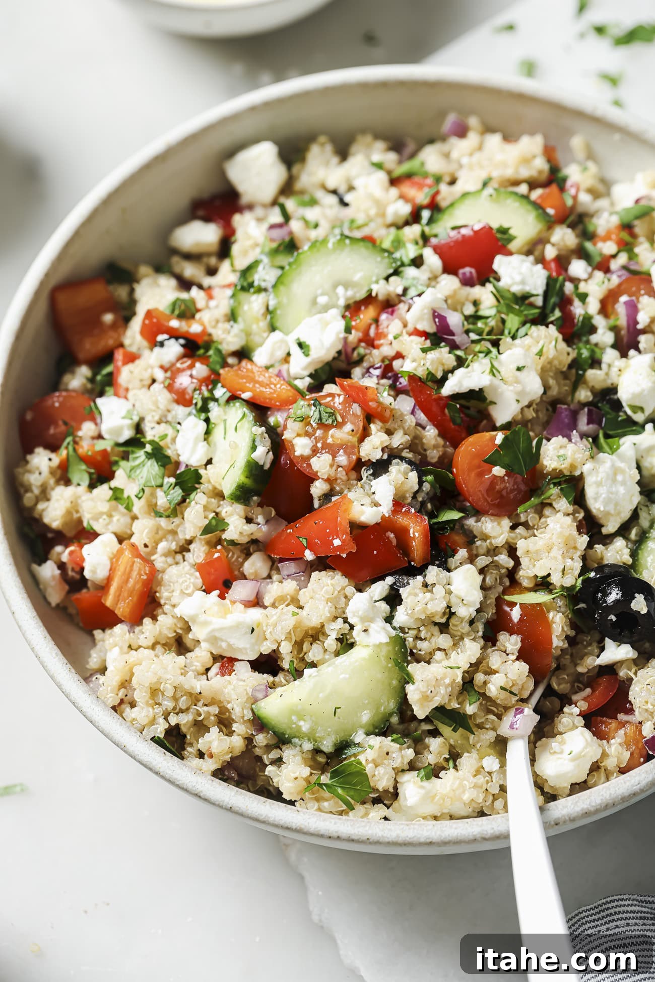 Close up of a freshly made Greek quinoa salad in a white bowl, ready to be served.