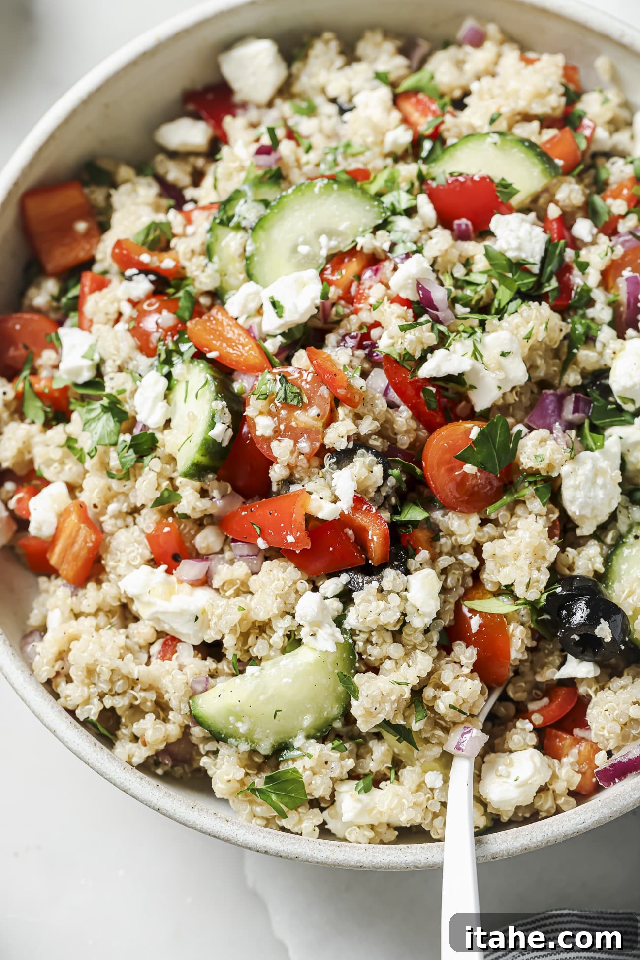 Close up of Greek quinoa salad in a white bowl, showing fresh ingredients and fluffy quinoa.