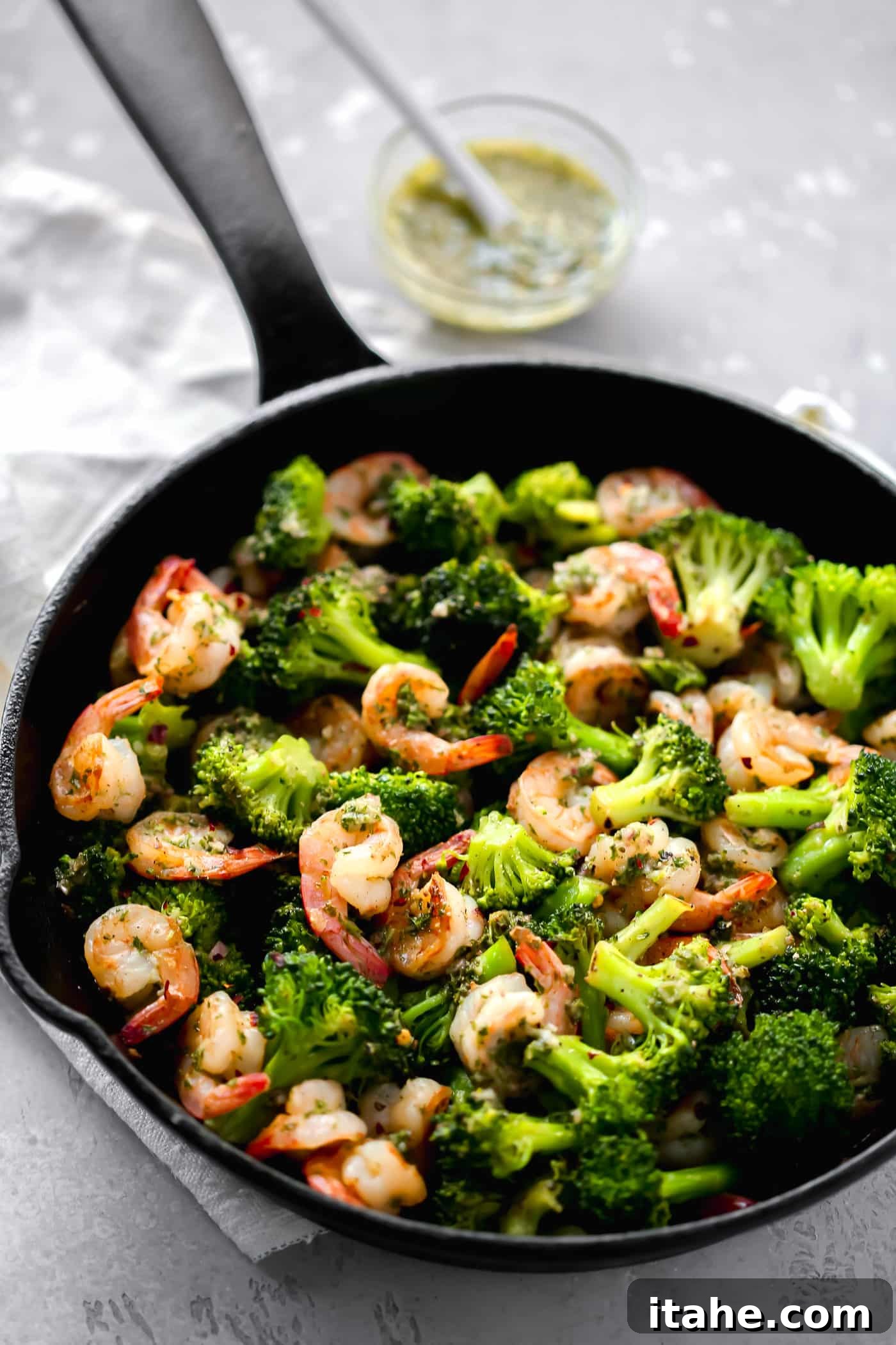 Effortless Keto Dinners 5 Close-up of perfectly cooked shrimp and vibrant broccoli coated in chimichurri sauce in a skillet.