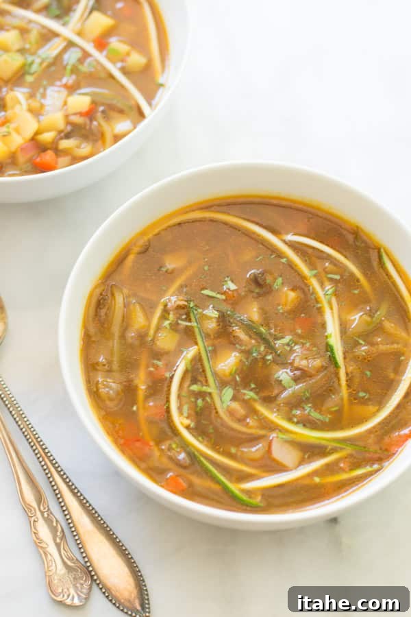 A bowl of fresh and flavorful zucchini noodle soup, garnished with herbs.