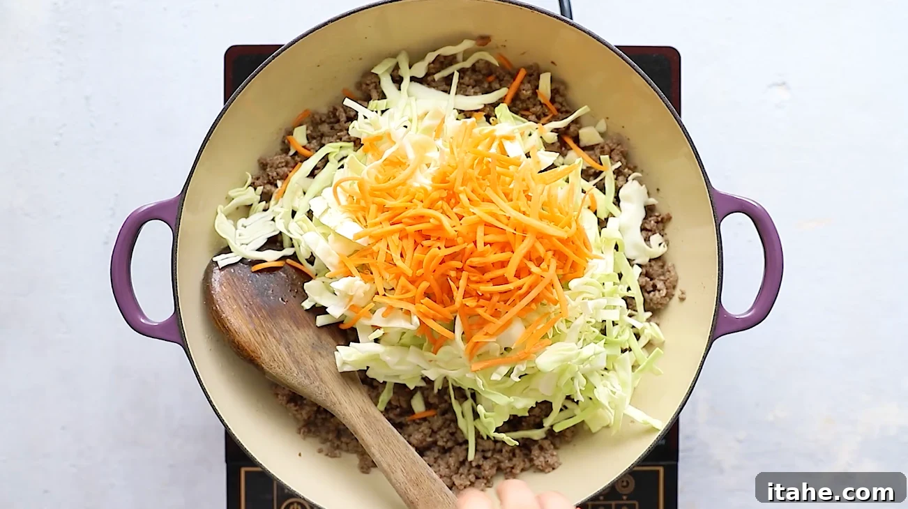 Unwrapped Egg Roll Bowl 4 Shredded cabbage and carrots added on top of cooked ground beef in a skillet.