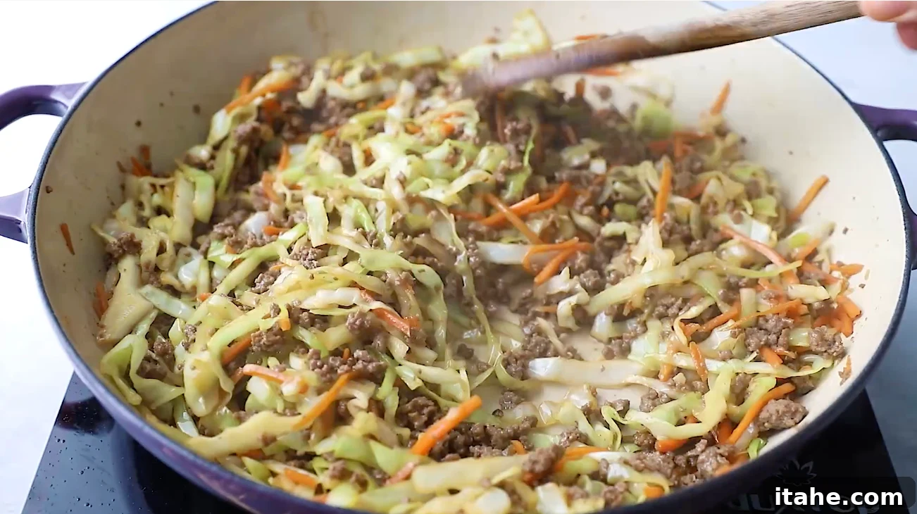 Unwrapped Egg Roll Bowl 5 Cooking ground beef in a skillet with a wooden spoon as the first step for making Egg Roll in a Bowl.