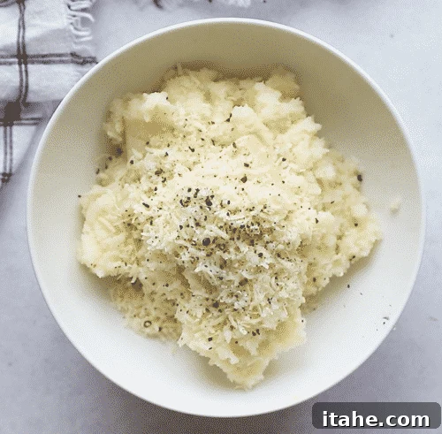 overhead view of a white bowl containing mashed cauliflower, parmesan and spices