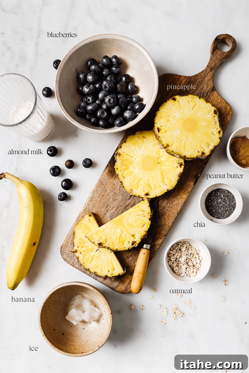 Various pre-measured ingredients for a blueberry banana smoothie, neatly arranged in small bowls and cups on a clean white countertop, ready for blending.