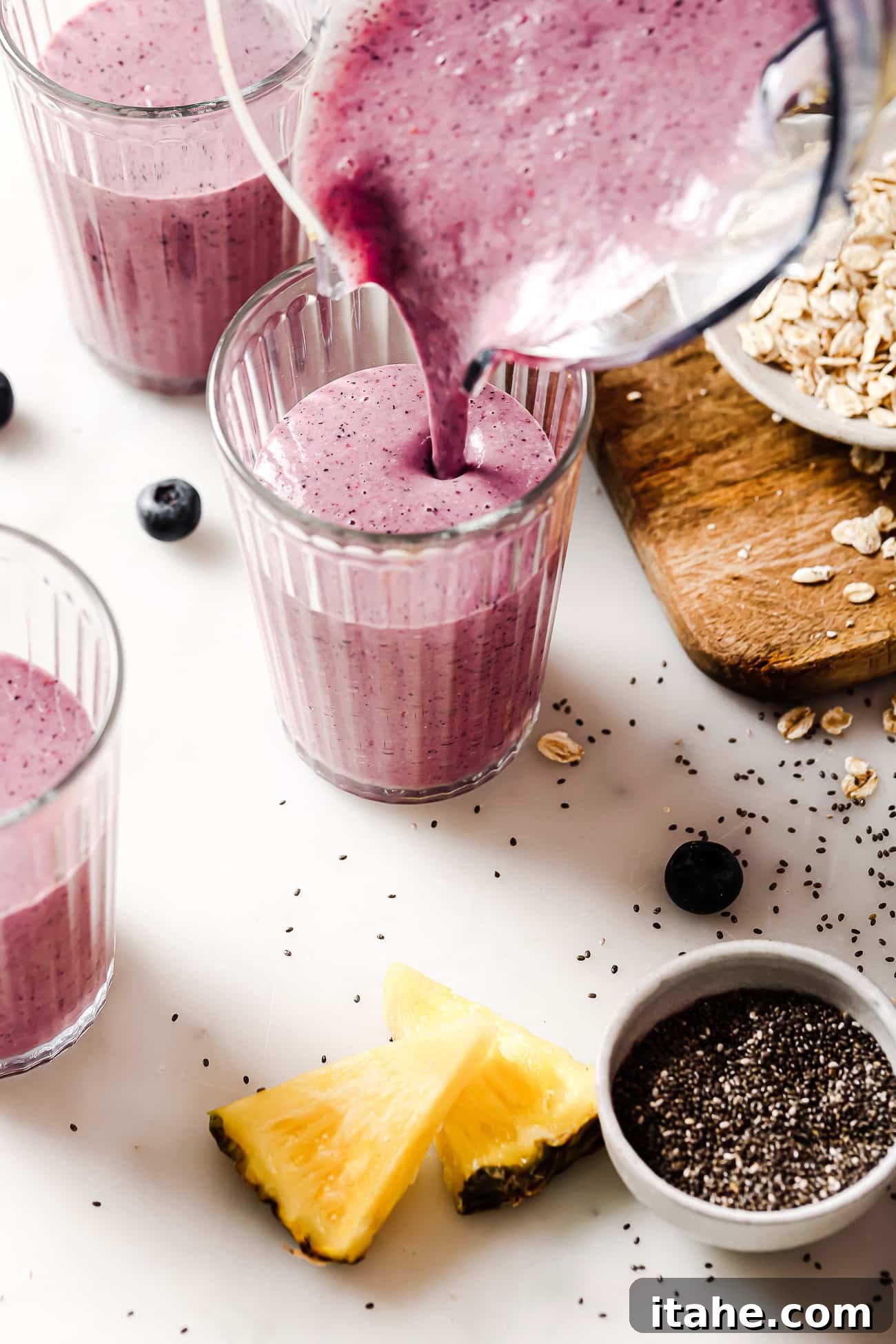 A stream of rich purple blueberry banana smoothie being poured from a sleek blender into a tall, clear glass, highlighting its creamy texture.