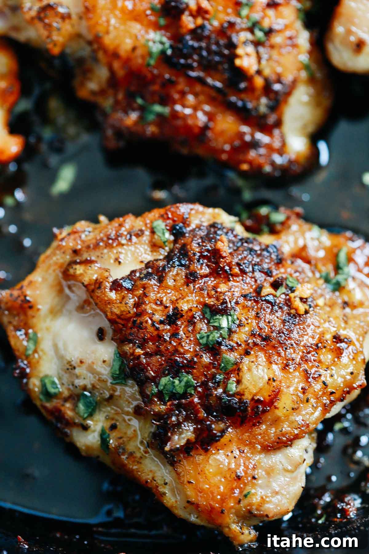 Close up of crispy chicken thighs in a cast iron skillet topped with fresh parsley