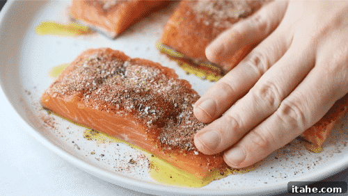 A close-up of salmon fillets being coated with dried spices on top.