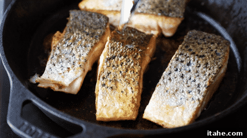 A close-up of crispy skin salmon cooking in a cast iron skillet.