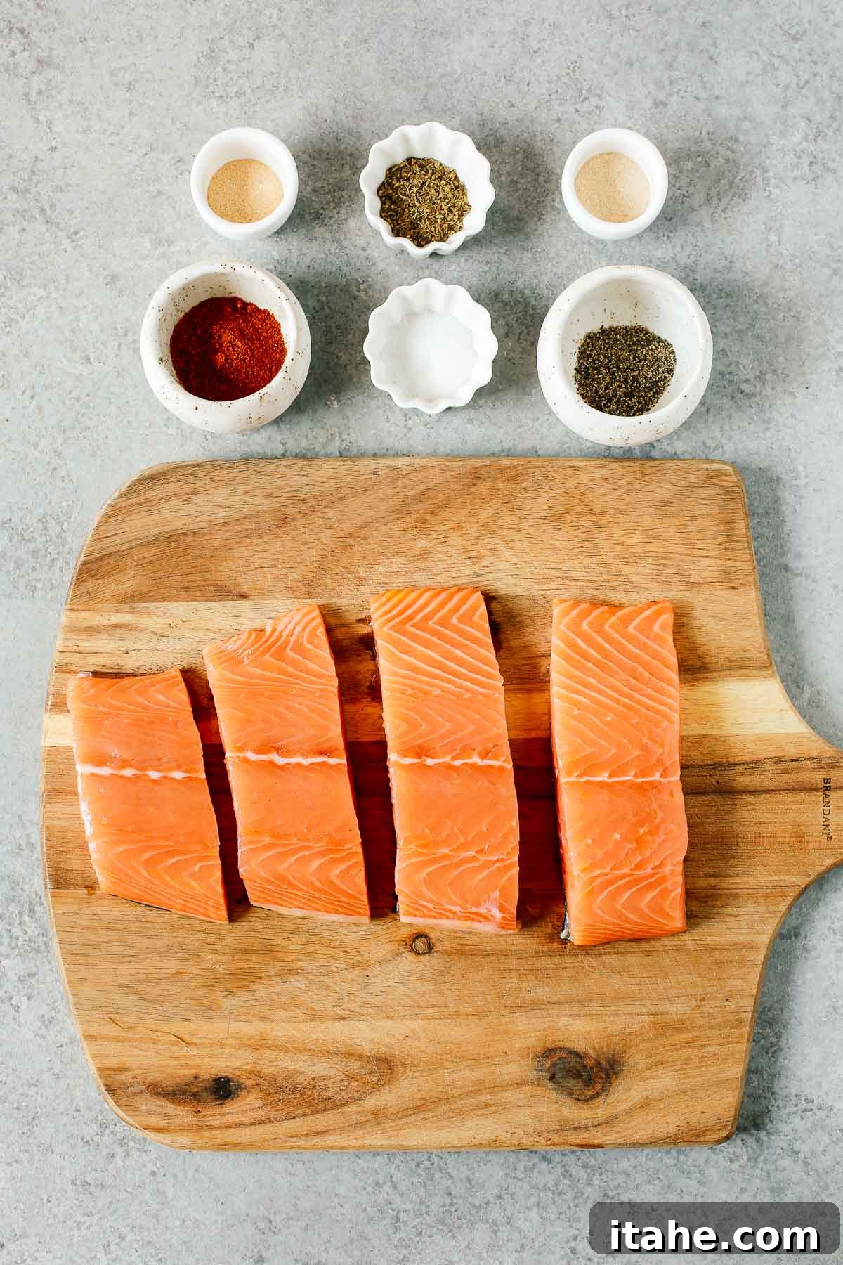 Overhead shot showcasing four raw salmon fillets alongside six small prep bowls filled with various spices, ready to be blended for a blackened salmon recipe.