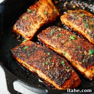 Four golden-brown and crispy blackened salmon fillets in a cast iron skillet.